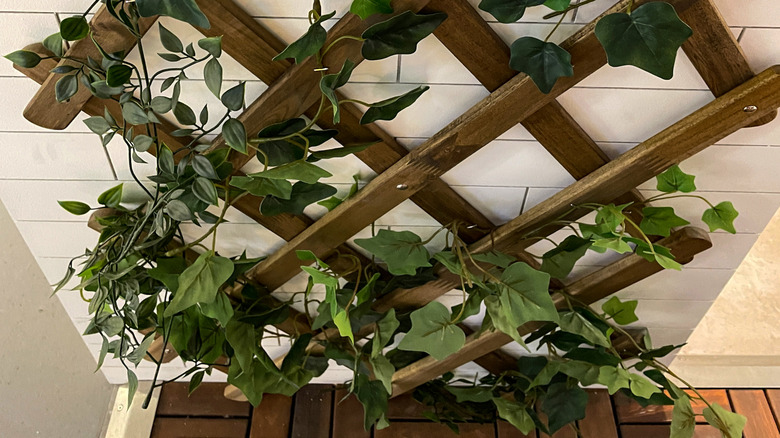 A white tile wall with a wooden trellis nailed to it with faux ivy vines.