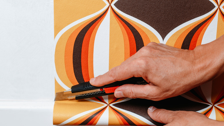 Man using utility knife to cut wallpaper