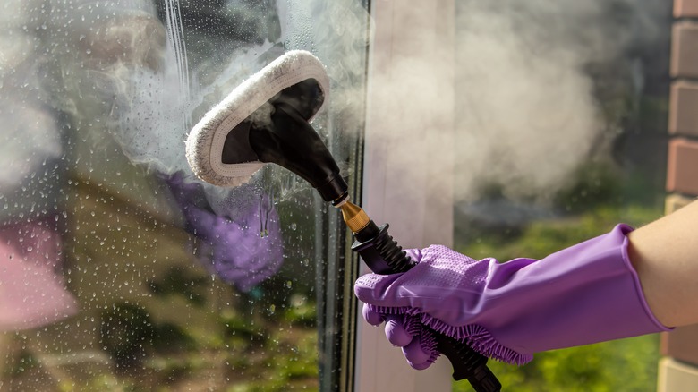 Purple-gloved hand steam cleaning a glass window.