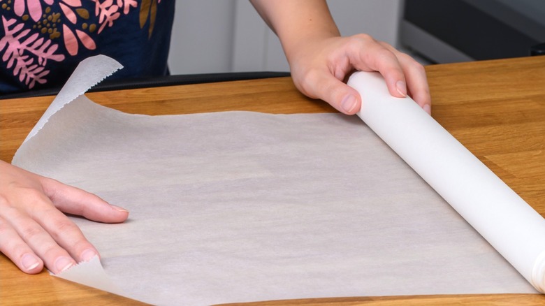 Person unrolling wax paper roll on wood counter