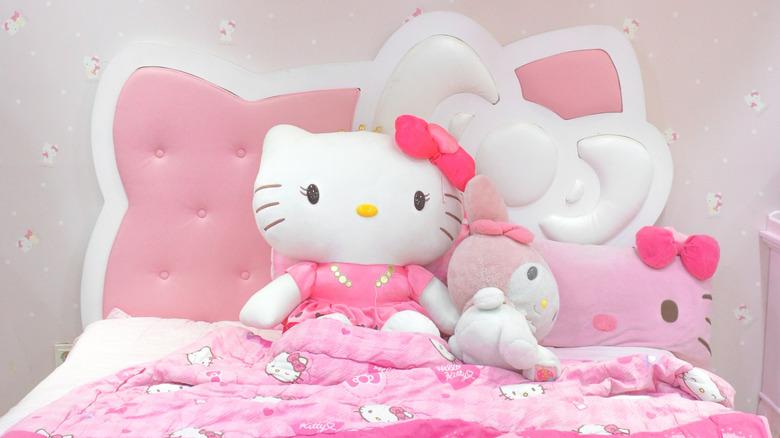A Hello Kitty and My Melody plushy on a cat shaped bed.