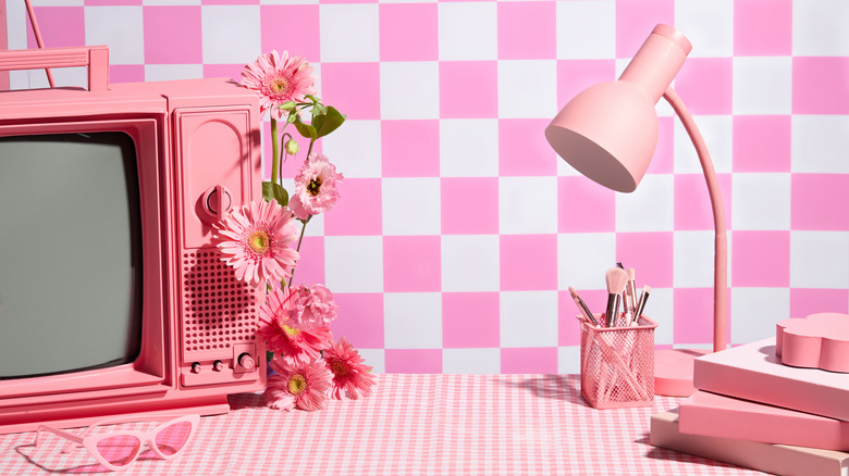 A pink lamp, flowers and television in front of a pink checkerboard background