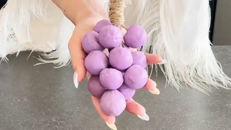 A woman holds a DIY bunch of soap grapes
