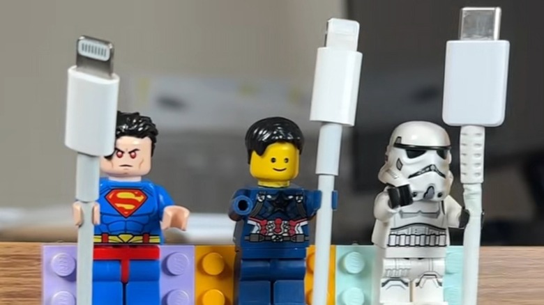 Closeup of three LEGO minifigurines (Evil Superman, Captain America, and a Stormtrooper) each holding a white cord, one lightning and two USB