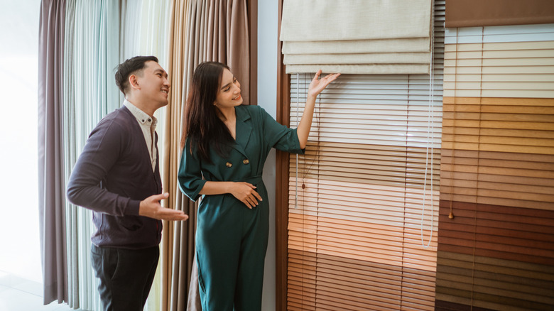 A female shopkeeper showing different window treatment options to a male customer
