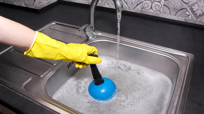Person with yellow rubber globe plunging a clogged sink
