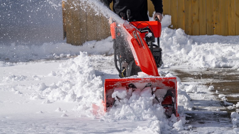 man using a red snow blower on a driveway