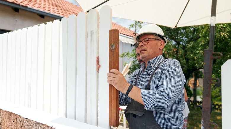 Carpenter building a white wooden fence