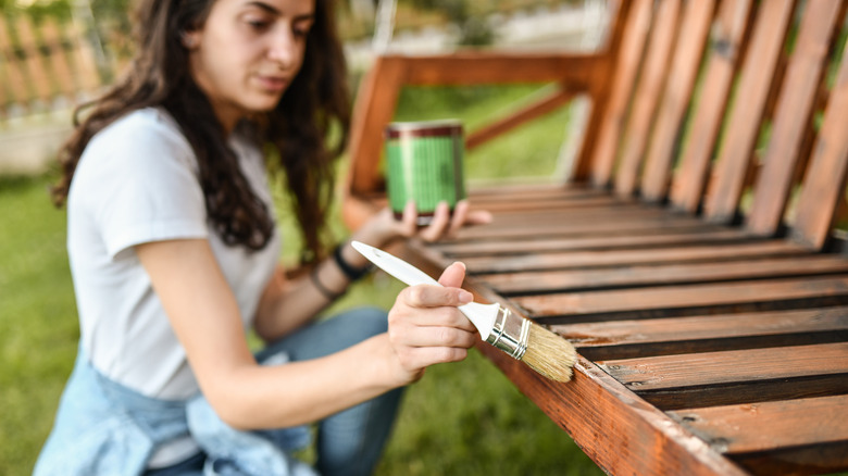 Woman applying sealant with a brush to an outdoor bench