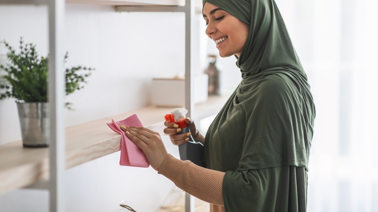 Woman cleaning bookshelf with spray