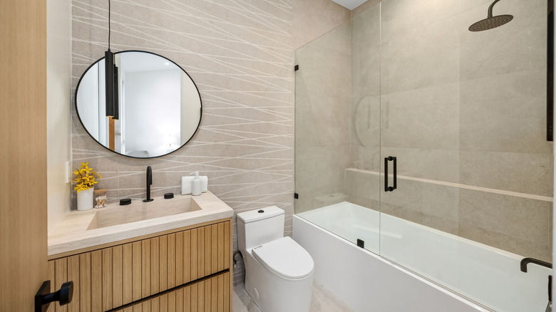 Modern bathroom with a round mirror, glass shower, and vanity in neutral tones