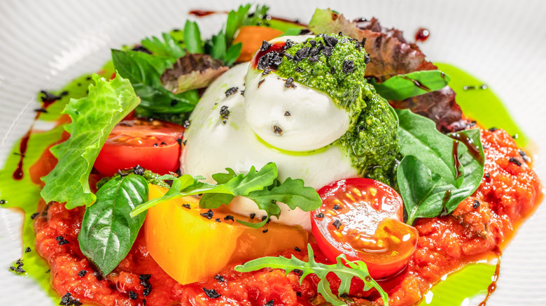 tomato sauce topped with chopped tomatoes, mozzella, greens, and green pesto