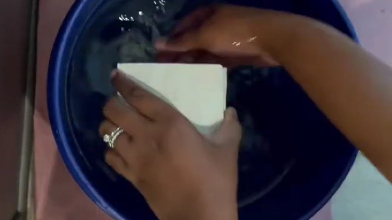 Hands soaking zellige tiles in bucket of water