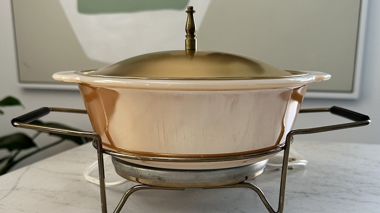 A vintage Fire King Atlantic Precision Works Warmer in Luster Peach with a lid and new cord on a wooden countertop.