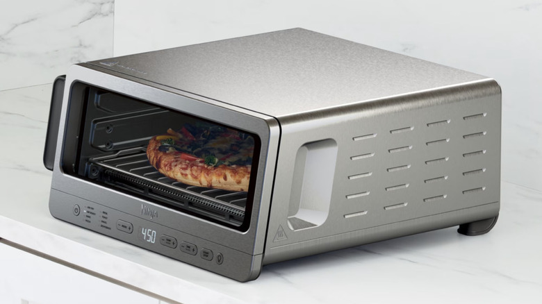 A brushed metal toaster oven and air fryer sitting on a white marble counter