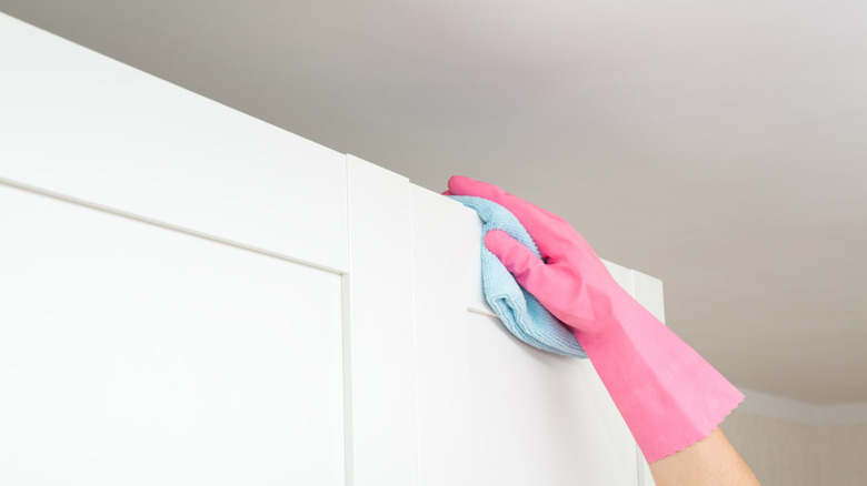 Close up of a woman dusting the top of a cabinet