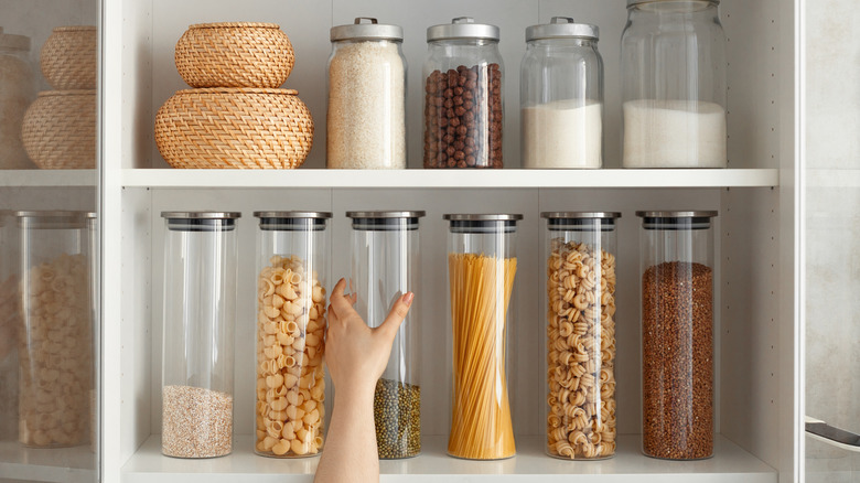 A person grabbing containers from open shelved cabinet