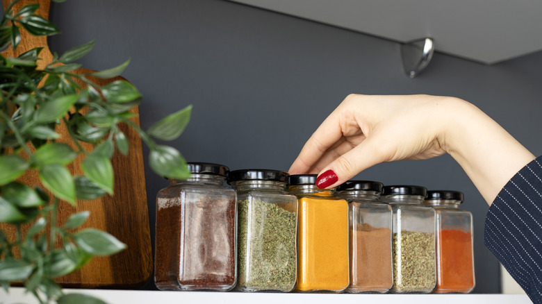 A person reaching for jars of spices in a kitchen