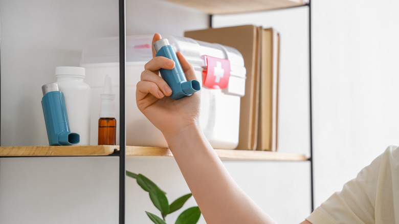 Person holding an inhaler in front of an open shelf with medicines and a first aid kit