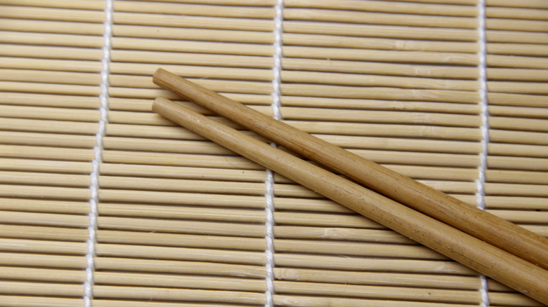 Wooden chopsticks resting on a bamboo mat.