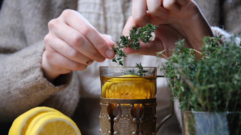 A person putting thyme twigs into a drink