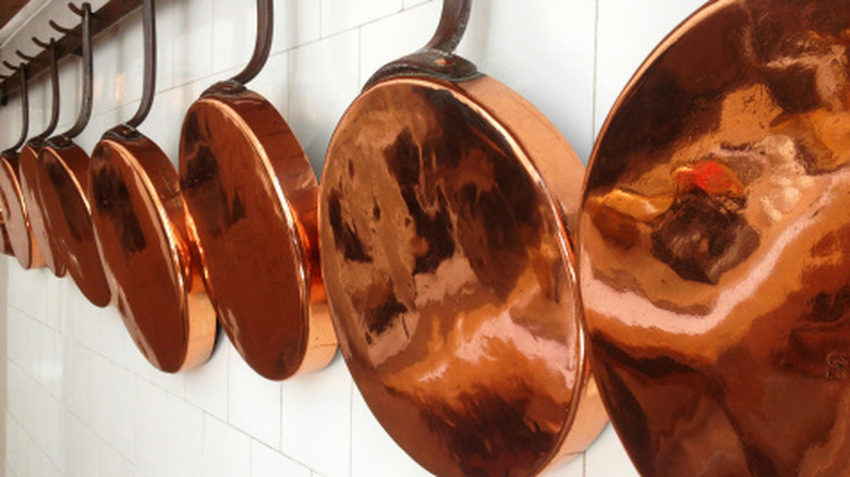 Copper frying pans hanging on a tiled wall