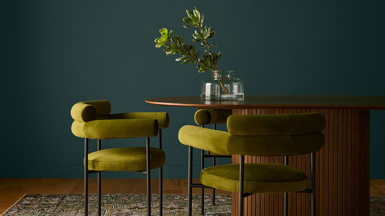 Chartreuse green chairs and a wooden table sit in front of a wall painted with Behr's 2026 Color of the Year Hidden Gem