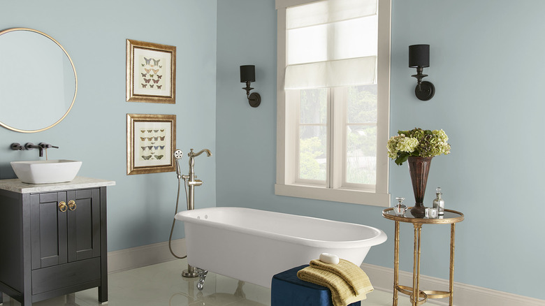 The walls of an elegant bathroom with a white clawfoot tub and gold hardware and accents is painted Behr's Watery