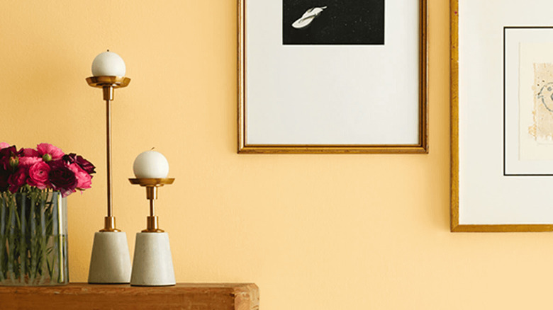 A vase full of pink flowers and two modern candlesticks sit in front of a wall painted Sherwin-Williams Classical Yellow