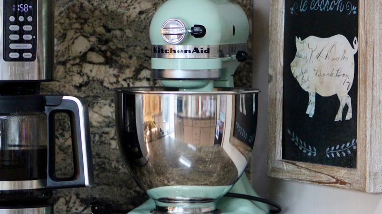 A teal KitchenAid with a metal bowl on top of a counter next to a coffee pot