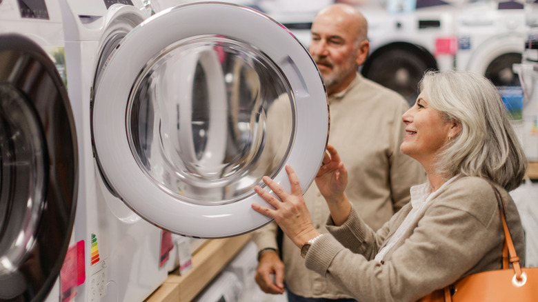 An elderly man and woman inspecting washers and dryers inside of a store