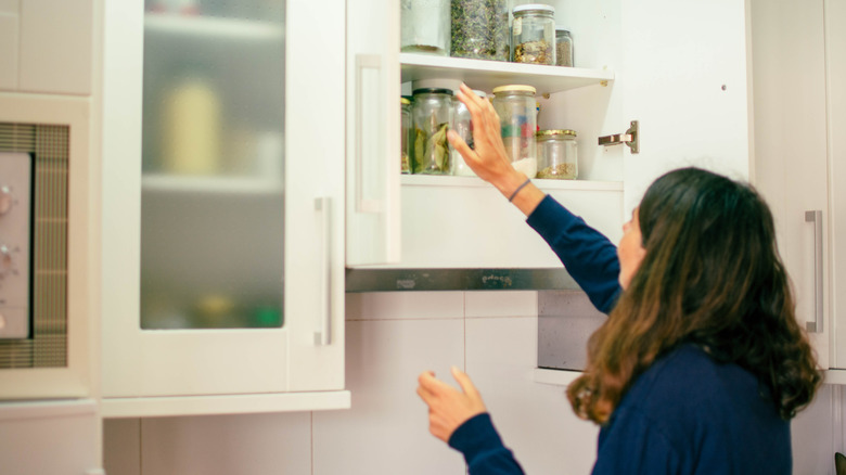 Woman reaching for items in jars in a cabinet
