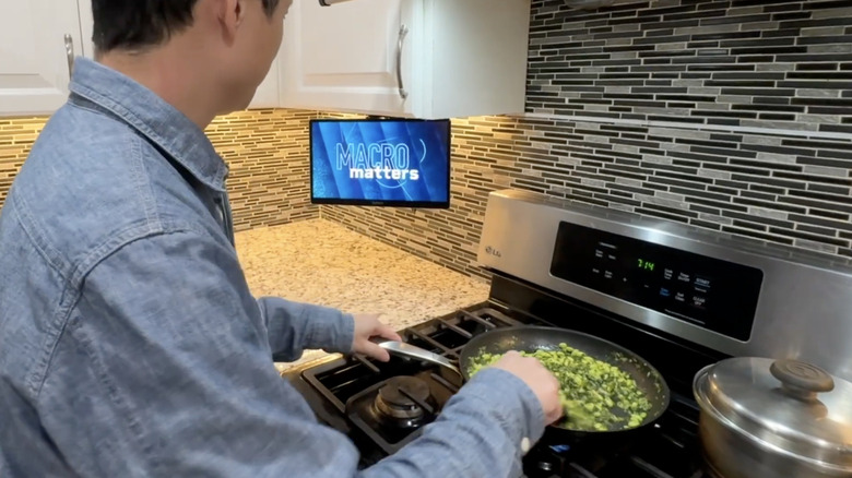 A TV next to a stove where a man is frying food