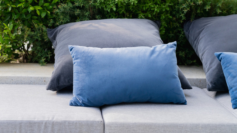blue pillows on gray couch on porch in front of bushes