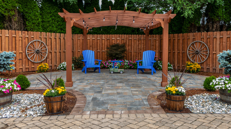 brown wood fence and awning on stone tile with truck decor, two wood wheels, and two blue chairs