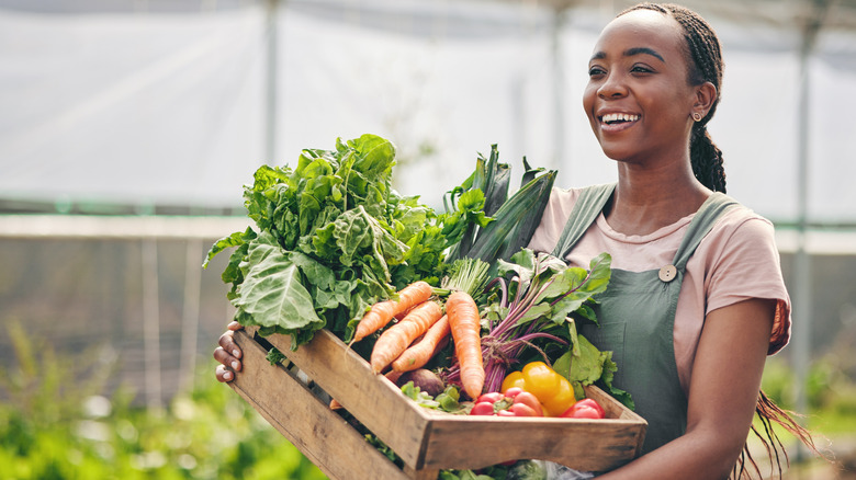 happy woman holding harvest box of vegetables