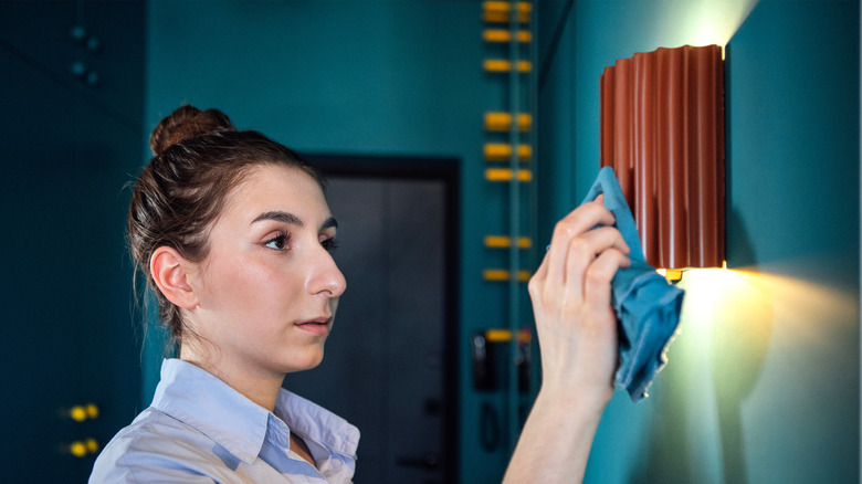 A woman uses a towel to wipe an orange wall sconce.