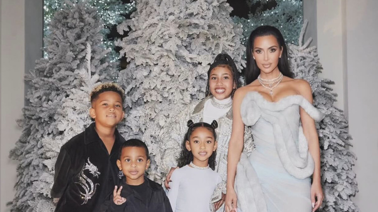 Kim Kardashian with her kids [L to R] Saint, Psalm, Chicago and North smiling for the cameras while standing in front of their white Christmas trees.