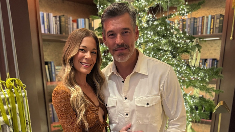 LeAnn Rimes and Eddie Cibrian smiling to the camera while posing in front of their Christmas tree.