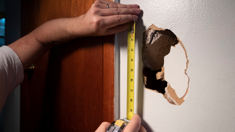 Hands measuring hole in wall