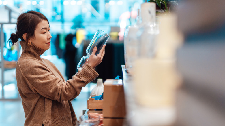 Woman is in a shop looking at a piece of glassware