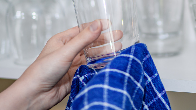 Hands polishing glassware with a blue striped towel