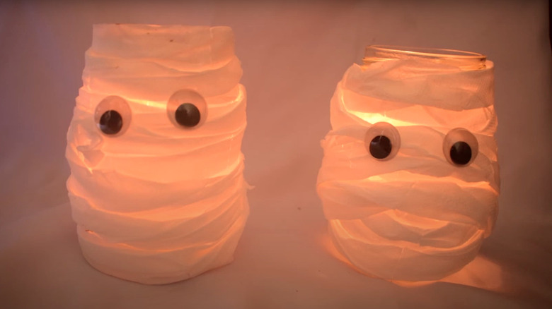 Two Halloween mason jar lanterns styled as mummies with googly eyes