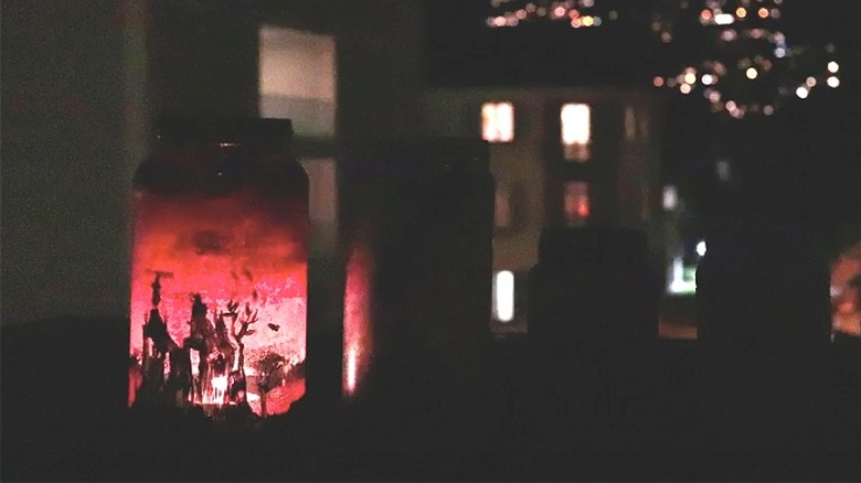 Halloween-themed mason jar lantern glowing in a drak space with city lights in the background