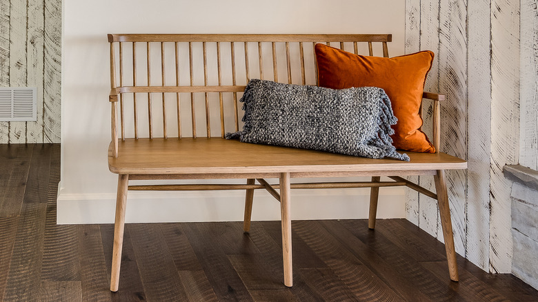 A wooden entryway bench with throw pillows on the seat