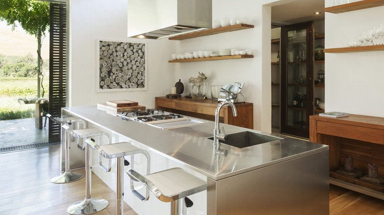 A modern kitchen with a stainless steel counterop on the island and wooden shelves.
