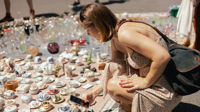 Woman taking photos of porcelain cups laid out on ground at a flea market