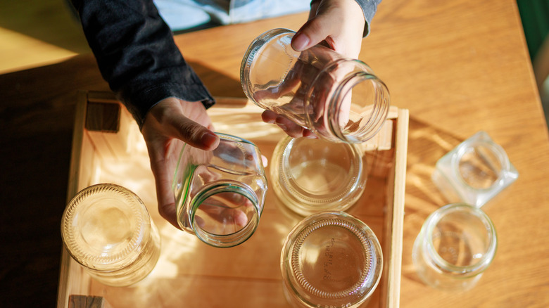 A person holding glass jars over a wood table with more glass jars on top.
