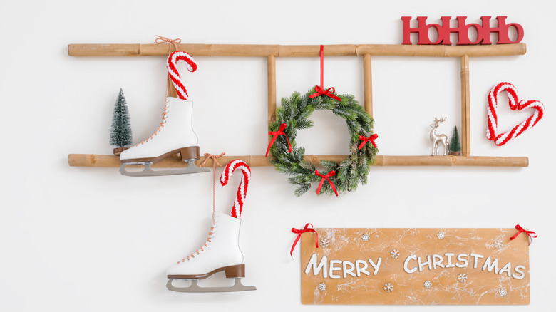 Ladder with Christmas wreath and ice skates on light wall