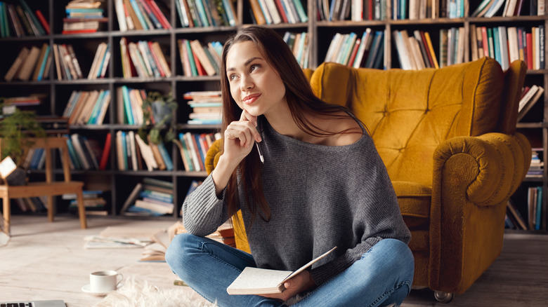 Young female in library sitting on the carpet looking up, thinking and smiling